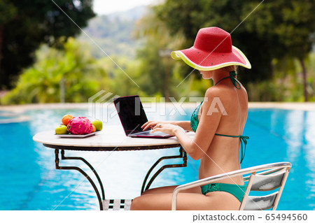 Woman with laptop at swimming pool. Remote work. 65494560