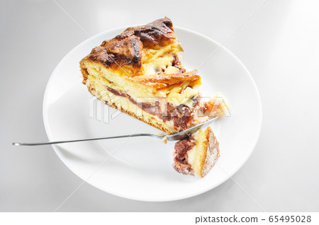 A piece of cake baked with cottage cheese and cherry on a white plate with a spoon. 65495028