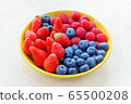 Strawberries raspberries blueberries in a yellow bowl on a light background, selective focus 65500208