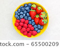 Berries in a yellow bowl on a light background, raspberries, strawberries, blueberries, top view 65500209