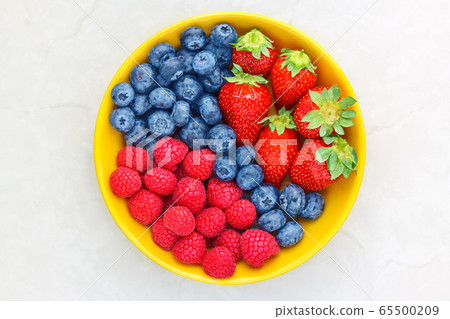 Berries in a yellow bowl on a light background, raspberries, strawberries, blueberries, top view Berries in a yellow bowl on a light background, raspberries, strawberries, blueberries, top view 65500209