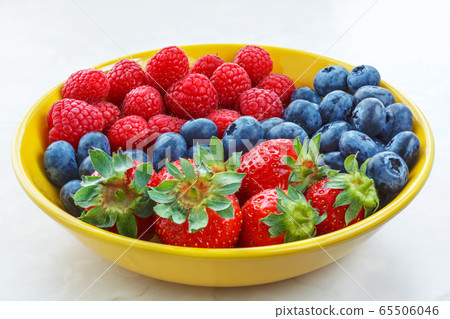 small fruit raspberries strawberries and blueberries close up in a yellow plate small fruit raspberries strawberries and blueberries close up in a yellow plate 65506046