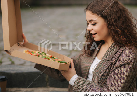 Woman open pizza box outdoors. Female hold open pizza box and smells appetizing 65507091