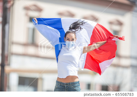 Female in a face mask holds a French flag on the 65508783