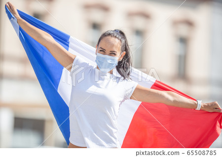 Female in a face mask holds a French flag on the 65508785