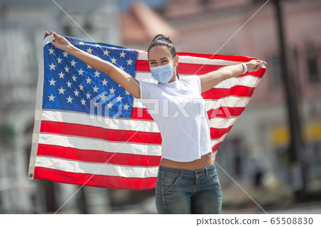 Young female in a face mask holding a US flag Young female in a face mask holding a US flag 65508830