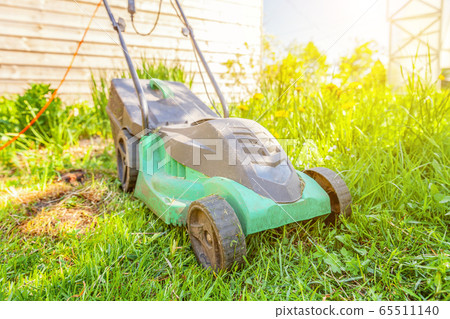 Lawn mower cutting green grass in backyard 65511140