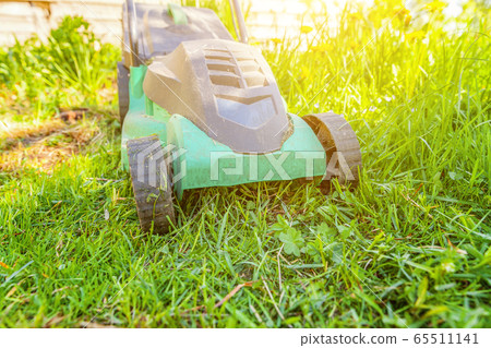Lawn mower cutting green grass in backyard 65511141