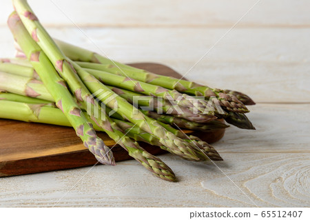 Raw fresh green asparagus stalks on a brown cutting board over a white wood kitchen table 65512407