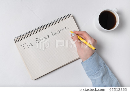 THE STORY BEGINS text in copybook. Female hands THE STORY BEGINS text in copybook. Female hands 65512863