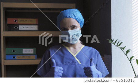 Thumbs up sign from a tired doctor. Female medical worker shows encouraging gesture meaning that everything will be fine. Pandemic 2020 concept Thumbs up sign from a tired doctor. Female medical worker shows encouraging gesture meaning that everything will be fine. Pandemic 2020 concept 65516313
