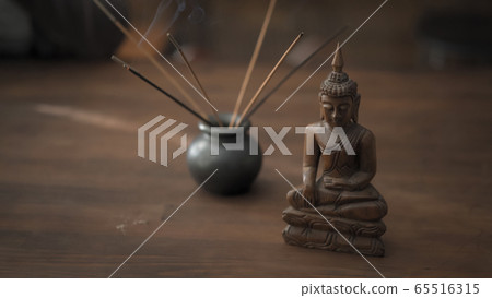 Workplace in oriental style with incense sticks and buddha statuette on a wooden table. Meditation concept Workplace in oriental style with incense sticks and buddha statuette on a wooden table. Meditation concept 65516315