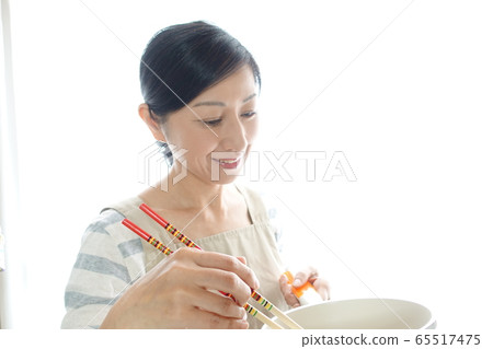 An image of a middle-aged woman in an apron cooking with a smile An image of a middle-aged woman in an apron cooking with a smile 65517475