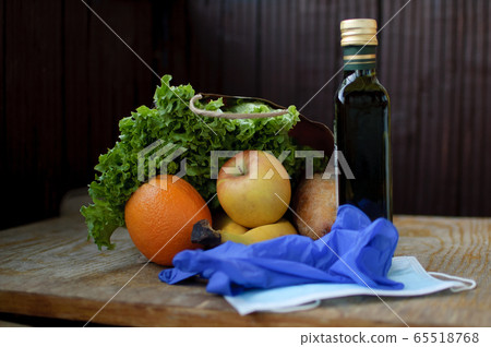 Product set on the wooden windowsill. Green leaves of the salad and fruits lying near surgical mask and blue protective gloves. Delivery food during a Coronavirus pandemic and isolation. Product set on the wooden windowsill. Green leaves of the salad and fruits lying near surgical mask and blue protective gloves. Delivery food during a Coronavirus pandemic and isolation. 65518768