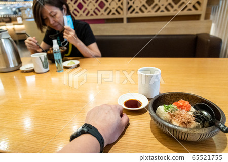 Perspective view and focus on meal, with another diner sitting diagonally across table 65521755