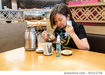 Asian women having meal with facemask and and sanitizer, with social distancing in Malaysia 65521756