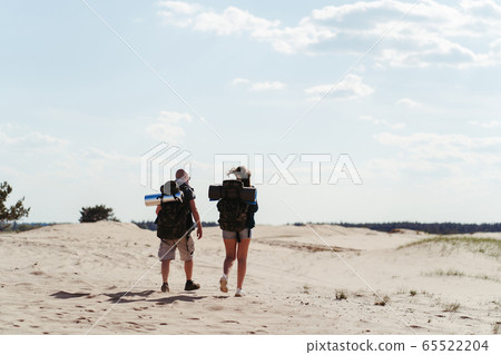 Tourists with backpacks traveling through desert 65522204
