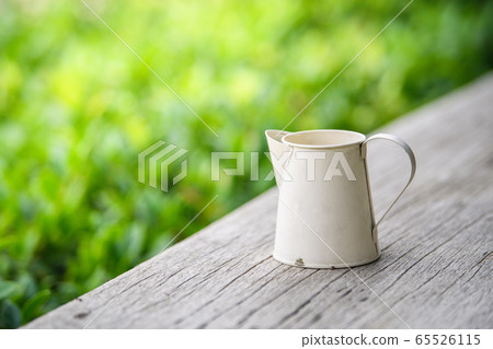 White zinc pitcher on a wooden table in the garden White zinc pitcher on a wooden table in the garden 65526115