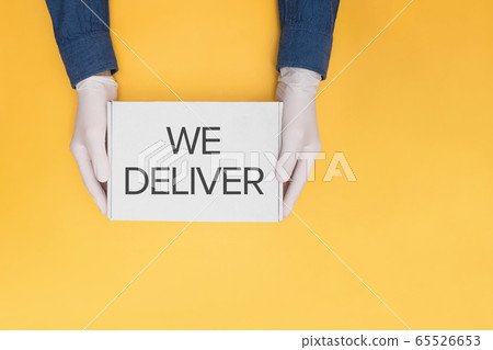 Courier's hands in protective gloves holding a cardboard with text We Deliver box 65526653