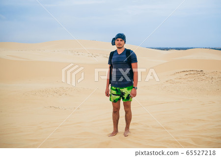 man tourist with a backpack and a bandana in the sandy desert man tourist with a backpack and a bandana in the sandy desert 65527218