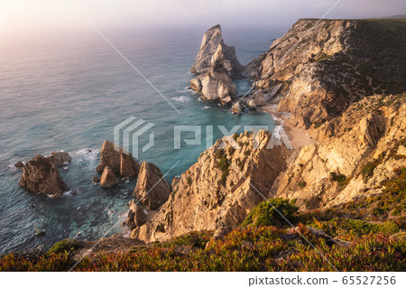 Sunset at Praia da Ursa Beach. Rocky cliff ridge with sea stack in atlantic ocean lit by evening warm light. Holiday vacation in Sintra region, Portugal 65527256