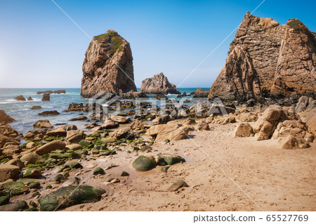 Rocks at Ursa beach, Sintra, Portugal. Epic sea stack towering at atlantic ocean coast lit by evening warm light Rocks at Ursa beach, Sintra, Portugal. Epic sea stack towering at atlantic ocean coast lit by evening warm light 65527769