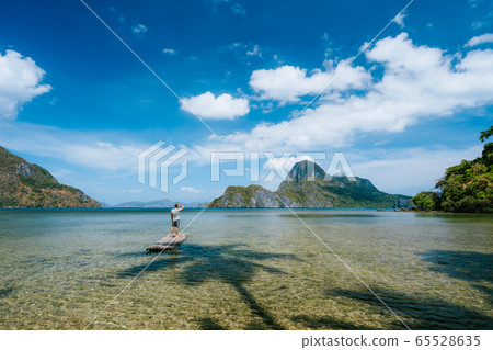 Man on bamboo float in shallow lagoon with panoramic view of shallow lagoon and Islands in Cadlao bay. Palawan, Philippines. Holiday vacation concept 65528635