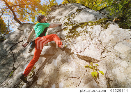 An aged bearded man is training in free climbing on a rock stone in the forest on a sunny day. The concept of leisure activities of an active lifestyle of people aged An aged bearded man is training in free climbing on a rock stone in the forest on a sunny day. The concept of leisure activities of an active lifestyle of people aged 65529544