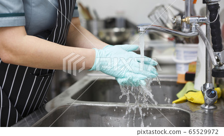 Woman in blue gloves washing hands thoroughly under water Woman in blue gloves washing hands thoroughly under water 65529972