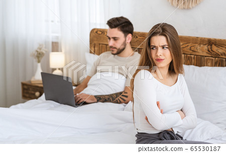 Man works on laptop, woman is offended by bed in bedroom. Man works on laptop, woman is offended by bed in bedroom. 65530187