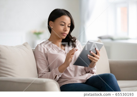 African woman sit on couch using tablet gadget African woman sit on couch using tablet gadget 65530193