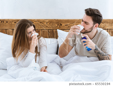 Cold and flu together concept. Husband and wife in bed wipe nose with napkin 65530194