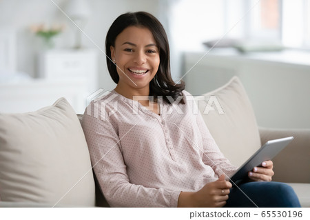 Happy african woman sitting on couch with tablet gadget Happy african woman sitting on couch with tablet gadget 65530196