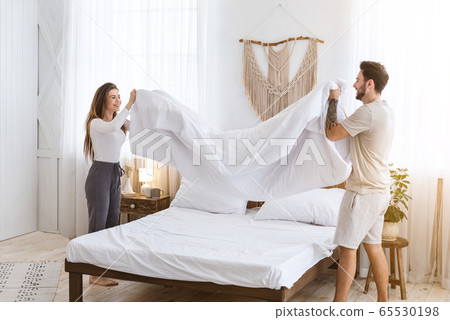 Couple making a bed together. Man and woman holding blanket in bedroom Couple making a bed together. Man and woman holding blanket in bedroom 65530198