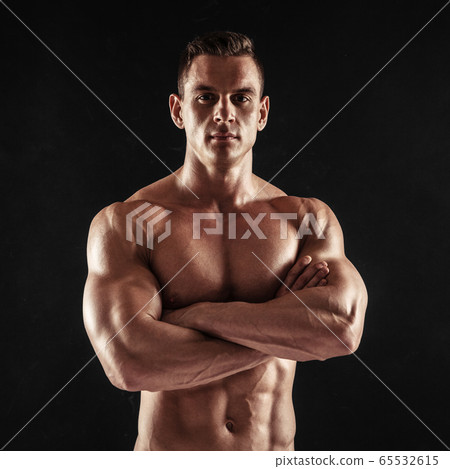Fitness in gym, sport and healthy lifestyle concept. Handsome athletic man showing his trained body on dark background. Bodybuilder male model standing with crossed hands and tight muscles. Fitness in gym, sport and healthy lifestyle concept. Handsome athletic man showing his trained body on dark background. Bodybuilder male model standing with crossed hands and tight muscles. 65532615