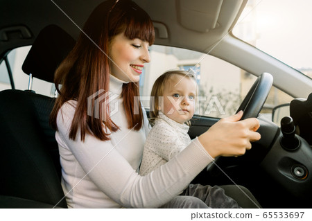 Mother with little baby girl sitting in front seat and driving car together. Child in danger, no safety on the road 65533697