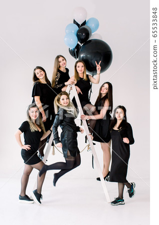 Happy young seven girls in black dresses having fun celebrating birthday in light room. The friends having fun posing on the ladder, decorated with colorful air balloons. Happy young seven girls in black dresses having fun celebrating birthday in light room. The friends having fun posing on the ladder, decorated with colorful air balloons. 65533848