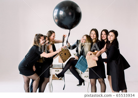 Pretty girl sitting on the vintage table and holding big black balloon. Her beautiful six friends giving presents and having fun. Birthday party concept, holiday Pretty girl sitting on the vintage table and holding big black balloon. Her beautiful six friends giving presents and having fun. Birthday party concept, holiday 65533934