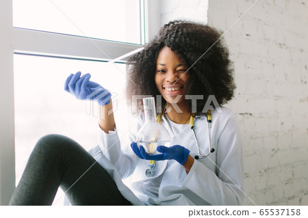 African American girl doctor in a white coat with a stethoscope. sitting at a table with reagent flasks on white background. Researcher researching in the laboratory African American girl doctor in a white coat with a stethoscope. sitting at a table with reagent flasks on white background. Researcher researching in the laboratory 65537158