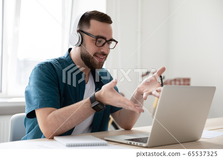 Smiling businessman in headphones looking at laptop screen watching webinar. 65537325