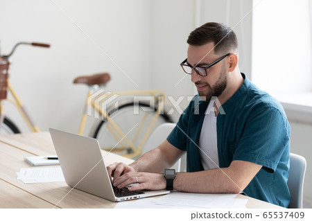 Happy young confident bearded businessman typing on keyboard using laptop. 65537409