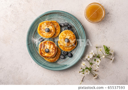Traditional russian cheesecake with blueberries and honey on a ceramic plate on a light background Traditional russian cheesecake with blueberries and honey on a ceramic plate on a light background 65537593