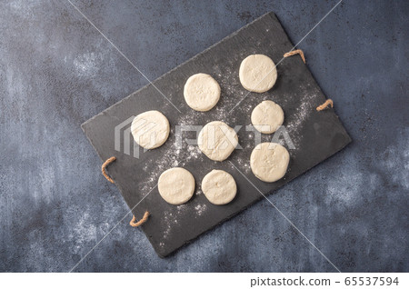 Cheesecakes semi-finished on a dark slate cutting board on a wooden background. Top view. Copy space Cheesecakes semi-finished on a dark slate cutting board on a wooden background. Top view. Copy space 65537594