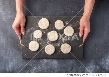 Women's hands hold cheesecakes semi-finished on a dark slate cutting board on a wooden background Women's hands hold cheesecakes semi-finished on a dark slate cutting board on a wooden background 65537595