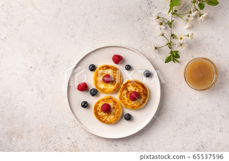 Traditional russian cheesecake with raspberries, blueberries and honey on a white ceramic plate on a Traditional russian cheesecake with raspberries, blueberries and honey on a white ceramic plate on a 65537596