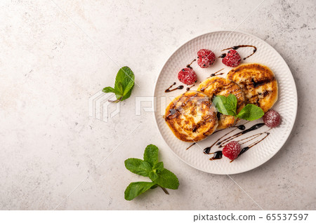 Homemade cheesecakes with raspberries, syrup and mint on a ceramic plate on a light wooden Homemade cheesecakes with raspberries, syrup and mint on a ceramic plate on a light wooden 65537597
