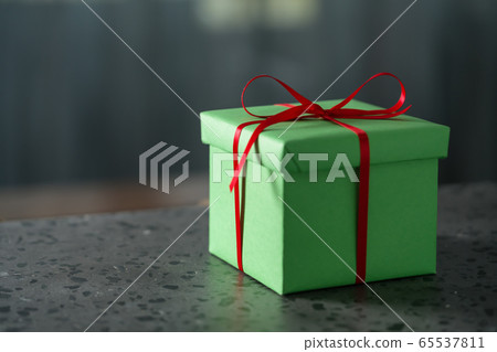 Green gift box with red ribbon against window on terrazo countertop with copy space Green gift box with red ribbon against window on terrazo countertop with copy space 65537811