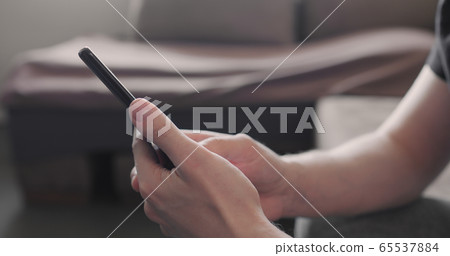 Closeup young man in black t-shirt typing messages on smartphone working from home side view 65537884
