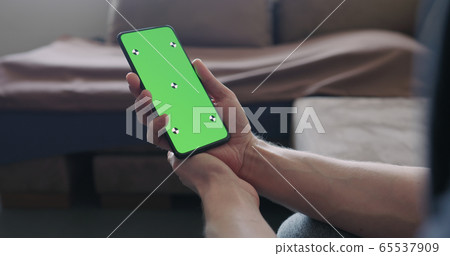 Closeup young man sit on a couch and watch something on a smartphone with green screen Closeup young man sit on a couch and watch something on a smartphone with green screen 65537909