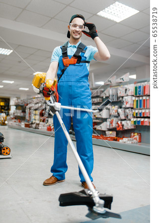Male worker holds gas trimmer in tool store Male worker holds gas trimmer in tool store 65538719